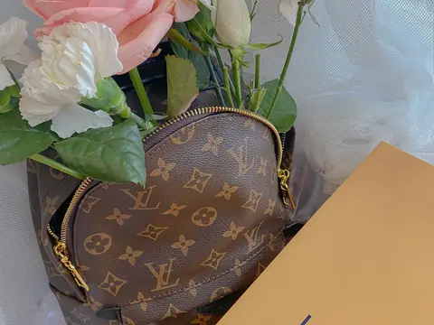 A Louis Vuitton monogram bag holding pink and white roses beside an orange Louis Vuitton box