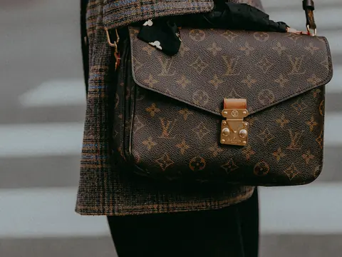 A Louis Vuitton Pochette Metis in monogram canvas worn crossbody over a check coat