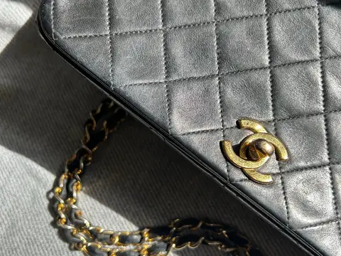 Close-up of a black quilted Chanel flap bag showing the gold CC turn-lock and leather-woven chain